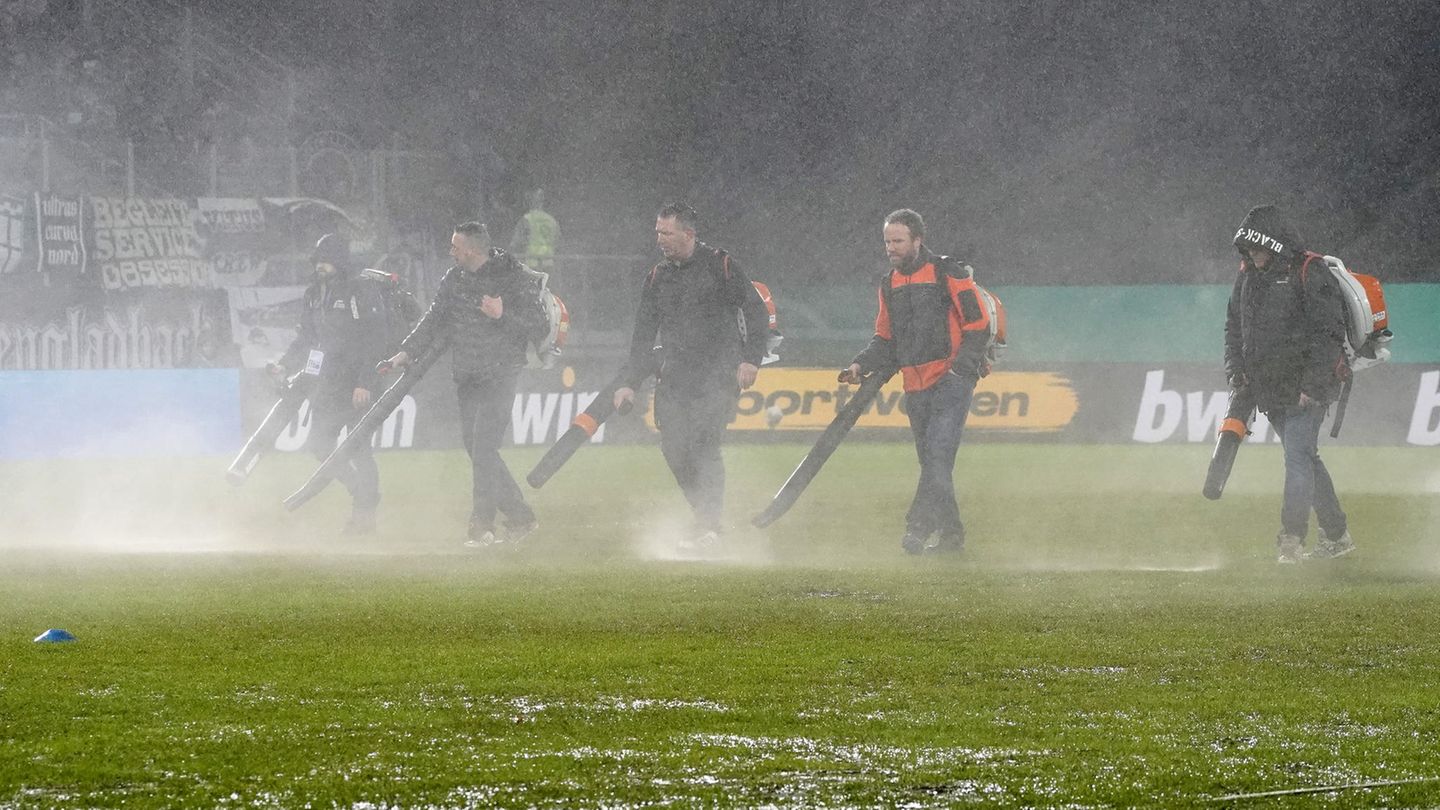 DFB-Pokal: Mit Laubbläsern versuchen Helfer, Wasser vom Rasen in Saarbrücken zu bekommen
