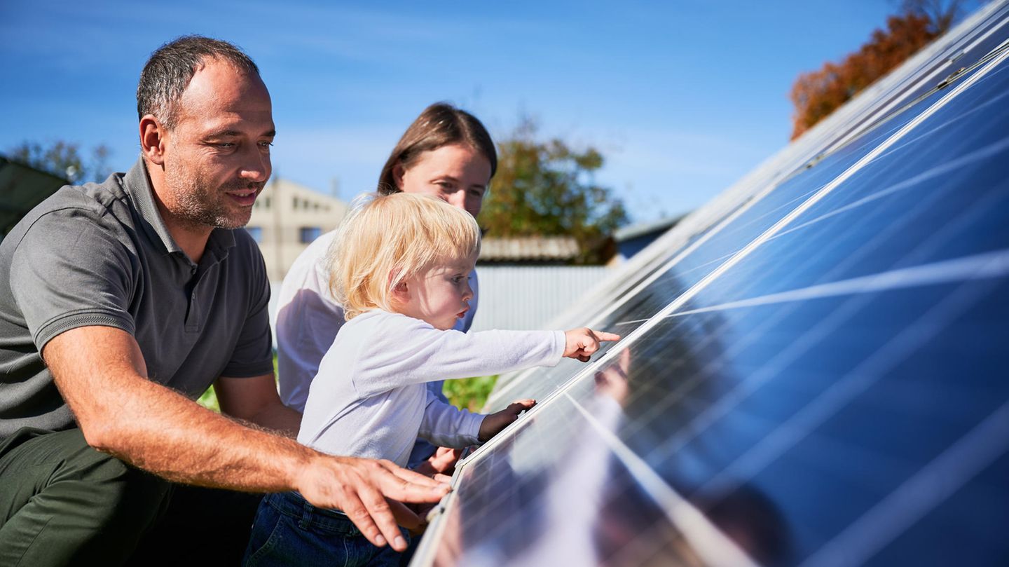 Wechselrichter: Vater, Mutter und Kind begutachten Solarmodule auf Hausdach