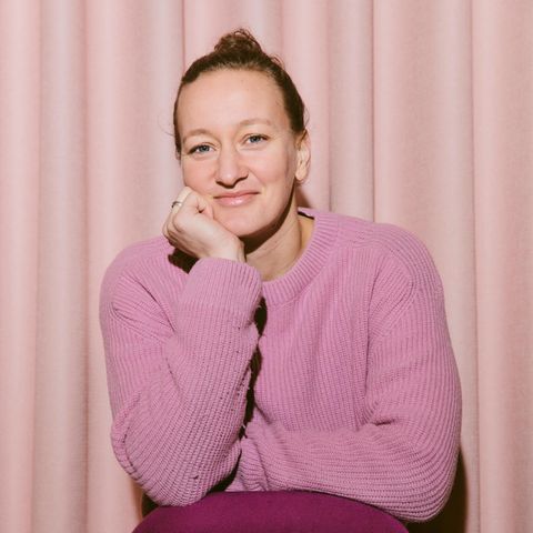 Eine Frau in einem rosa Pullover sitzt auf einem Stuhl und lächelt in die Kamera