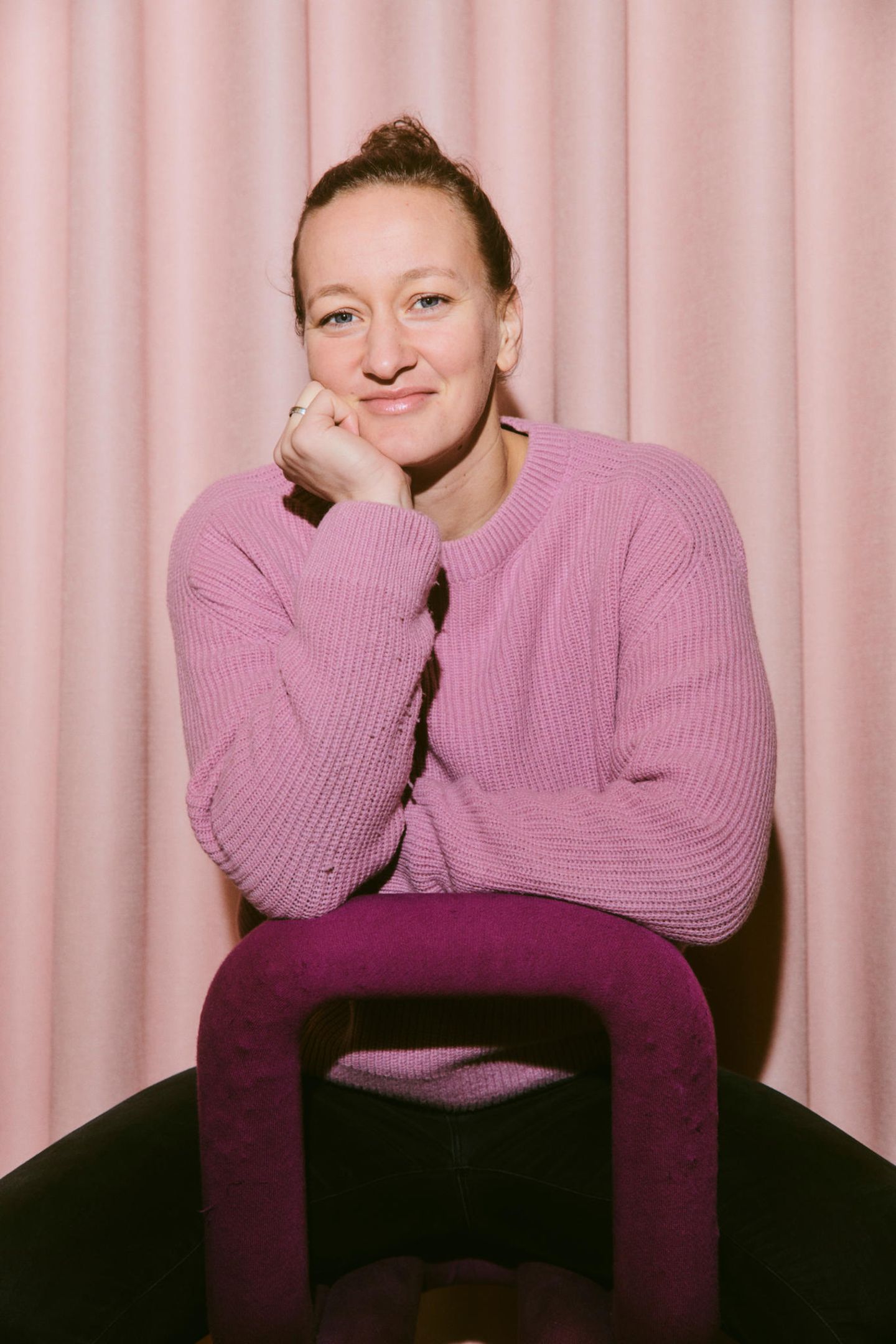 Eine Frau in einem rosa Pullover sitzt auf einem Stuhl und lächelt in die Kamera
