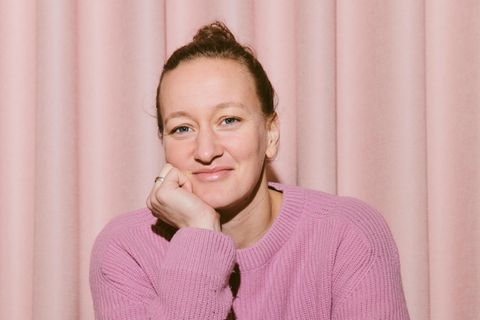 Eine Frau in einem rosa Pullover sitzt auf einem Stuhl und lächelt in die Kamera