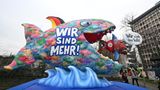 Ein bunter Fischschwarm mit der Aufschrift "Wir sind mehr" hat sich formiert und frisst einen blau-braunen Fisch