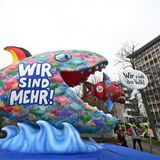 Ein bunter Fischschwarm mit der Aufschrift "Wir sind mehr" hat sich formiert und frisst einen blau-braunen Fisch