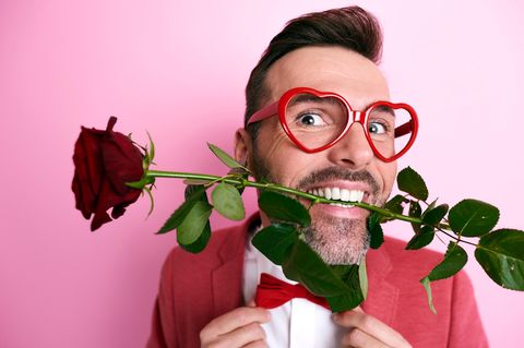 Valentinstag: Mann mit Herzchenbrille und Rose im Mund