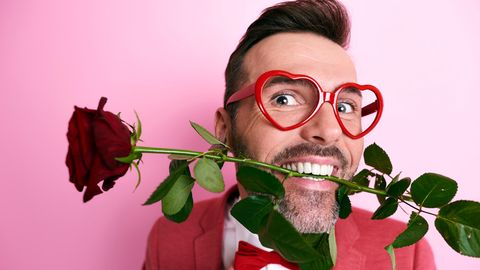 Valentinstag: Mann mit Herzchenbrille und Rose im Mund