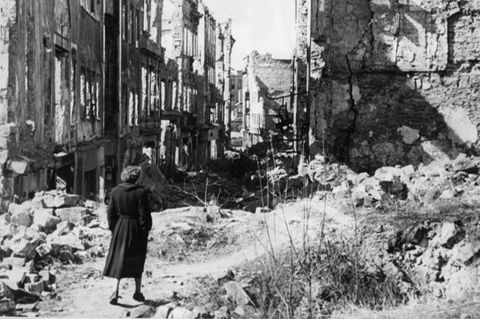 Eine Frau geht in einer Straße in Dresden an zerstörten Häusern vorbei.