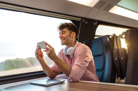 Junger Mann im ICE am Handy, freut sich über Allnet-Flat im Vodafone-Netz.
