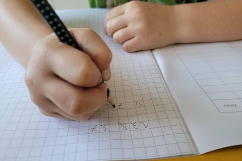 Schulabbruch: Eine Kinderhand schreibt Hausaufgaben in ein Schulheft