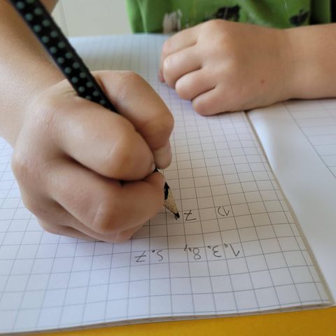 Schulabbruch: Eine Kinderhand schreibt Hausaufgaben in ein Schulheft