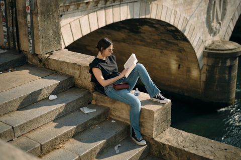 Frau sitzt mit einem Buch an der Seine in Frankreich