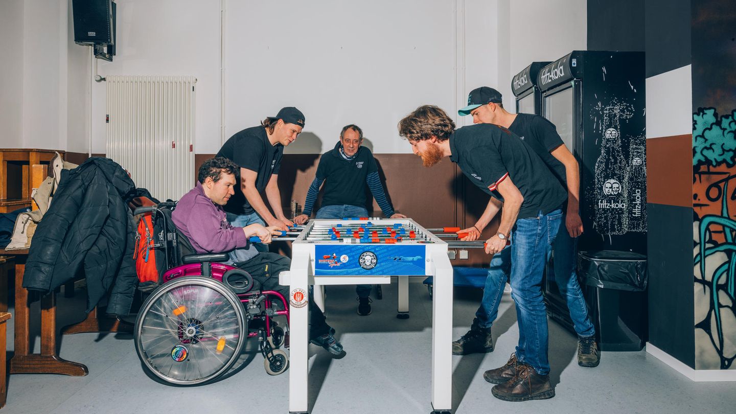 Eine Gruppe Männer, einer im Rollstuhl, spielen Tischfußball und haben Spaß.