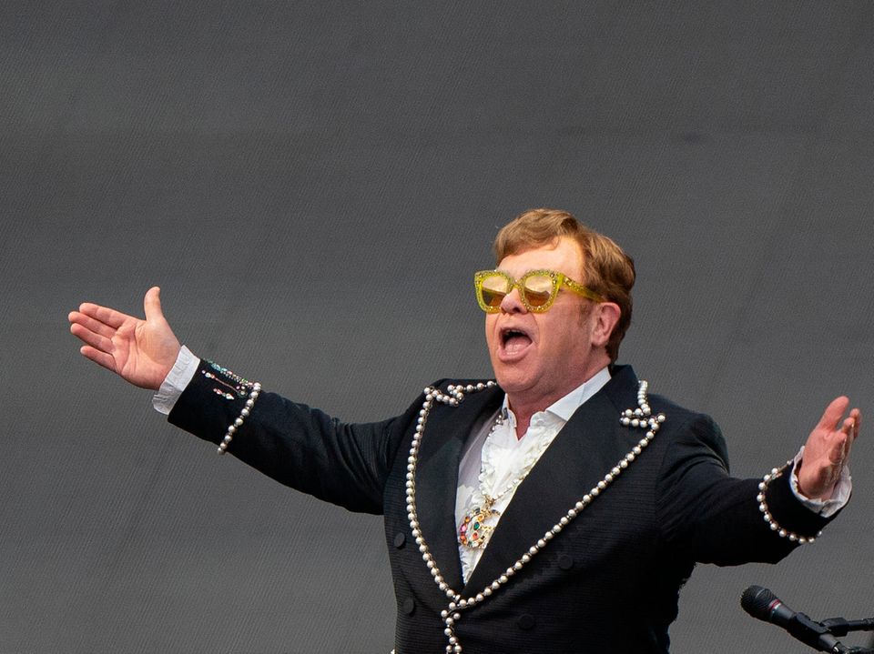 Elton John breitet bei einem Konzert auf der Bühne seine Arme aus