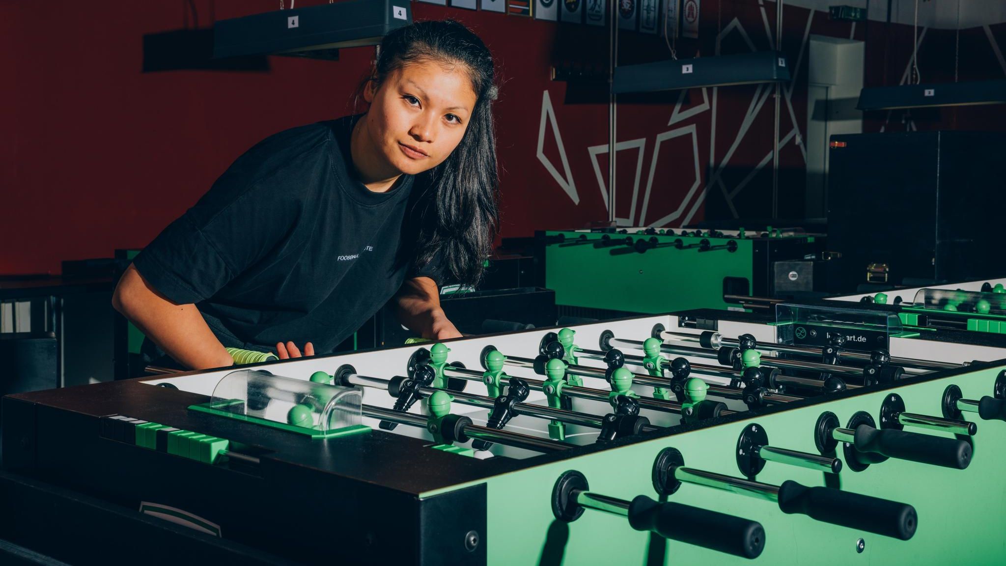 Linh Tran an einem Tischfußball leicht vorgebeugt in die Kamera blickend
