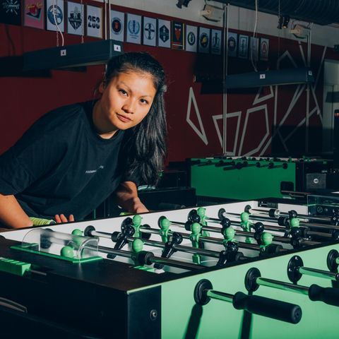 Linh Tran an einem Tischfußball leicht vorgebeugt in die Kamera blickend
