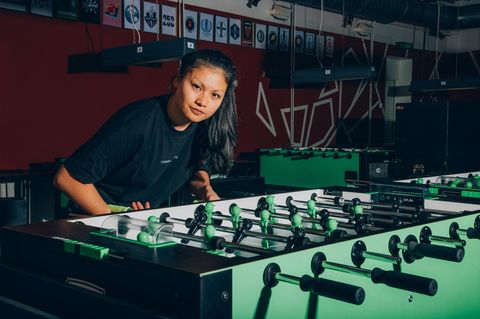 Linh Tran an einem Tischfußball leicht vorgebeugt in die Kamera blickend