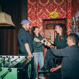 4er Gruppe stöst mit Flaschenbier an und steht am Tischfußball