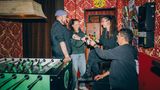 4er Gruppe stöst mit Flaschenbier an und steht am Tischfußball