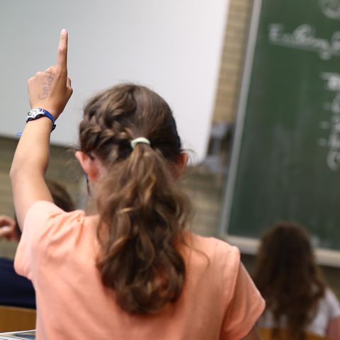 Symbolfoto für AfD-Parolen in der Schule: Eine Schülerin sitzt im Klassenraum und hebt die Hand