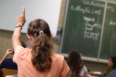 Symbolfoto für AfD-Parolen in der Schule: Eine Schülerin sitzt im Klassenraum und hebt die Hand
