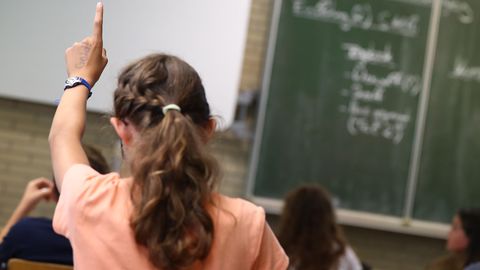 Symbolfoto für AfD-Parolen in der Schule: Eine Schülerin sitzt im Klassenraum und hebt die Hand