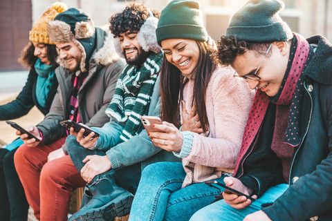 Gutscheinaktion: Junge Leute sitzen mit Smartphone auf einer Mauer und freuen sich.