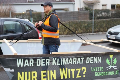 Aktivist der "Letzten Generation" trägt ein Holzgestell in SUV-Größe