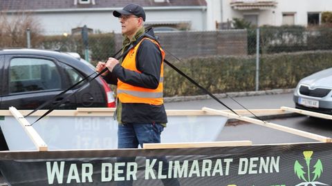 Aktivist der "Letzten Generation" trägt ein Holzgestell in SUV-Größe