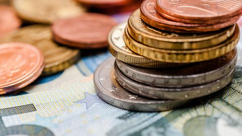 Grundsicherung in der Rente: Ein Stapel Geldmünzen liegt auf einem 5-Euro-Schein