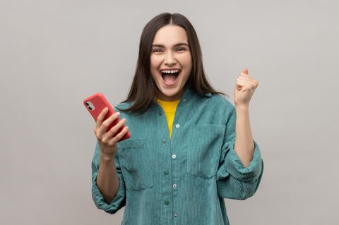 Symbolbild "Wordle": Eine Spielerin mit Handy in der Hand freut sich über ihren Erfolg