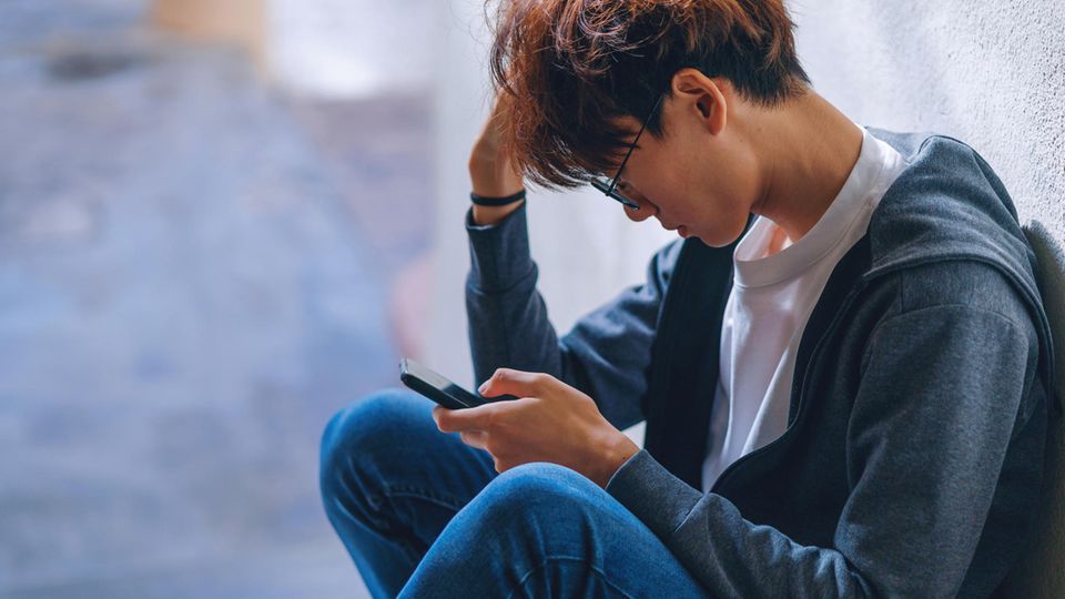 Symbolfoto zum Thema Dating: Ein junger Mann schaut frustriert auf sein Handy