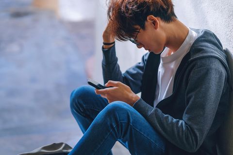 Symbolfoto zum Thema Dating: Ein junger Mann schaut frustriert auf sein Handy