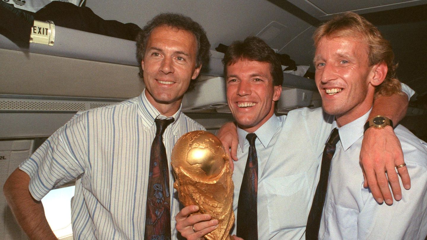 Im Flugzeug auf dem Rückflug von Rom nach Frankfurt zeigen Teamchef Franz Beckenbauer (l.), Kapitän Lothar Matthäus (M.) und Andreas Brehme den WM-Pokal. Mit Beckenbauer verbindet Brehme in den Jahren danach eine enge Freundschaft.