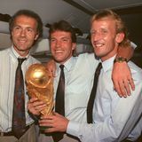 Im Flugzeug auf dem Rückflug von Rom nach Frankfurt zeigen Teamchef Franz Beckenbauer (l.), Kapitän Lothar Matthäus (M.) und Andreas Brehme den WM-Pokal. Mit Beckenbauer verbindet Brehme in den Jahren danach eine enge Freundschaft.