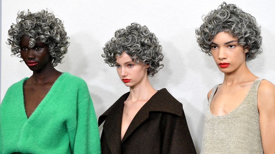 Three models with gray curly wigs backstage at JW Anderson