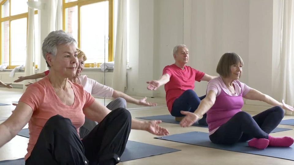 Ältere Personen sitzen in einer Turnhalle und machen Sportübungen.