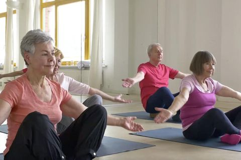 Ältere Personen sitzen in einer Turnhalle und machen Sportübungen.