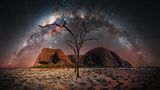 Der Ayers Rock vor einem Sternenhimmel, die Milchstraße zieht einen Bogen über den Horizont