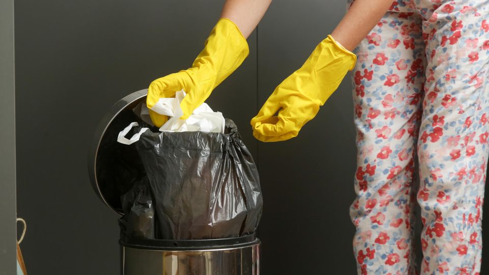Eine Frau zieht eine volle Tüte aus einem Mülleimer