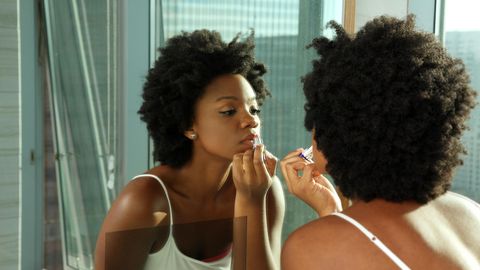Fenty Beauty by Rihanna: Eine Frau schminkt sich vor dem Spiegel.