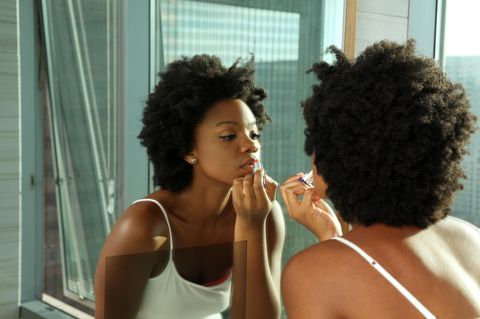 Fenty Beauty by Rihanna: Eine Frau schminkt sich vor dem Spiegel.