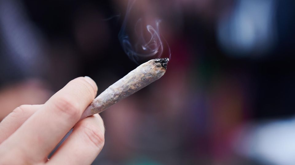 Eine rechte Hand hält einen rauchenden Joint – Cannabis wird in Deutschland legalisiert