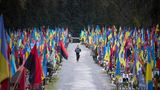 Lviv, Ukraine. Eine Frau geht den Hauptweg des Lychakiv-Friedhofs entlang. Links und rechts sind die Gräber von Gefallenen aus zwei Jahren Verteidigung gegen den russischen Angriff mit National- und Militärflaggen geschmückt. Ob bei Freunden und Angehörigen der Toten wohl die Trauer oder der Stolz überwiegt?