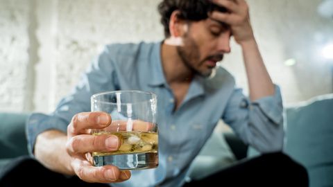 Ein Mann hält sich mit einem Glas Alkohol in der Hand den Kopf fest