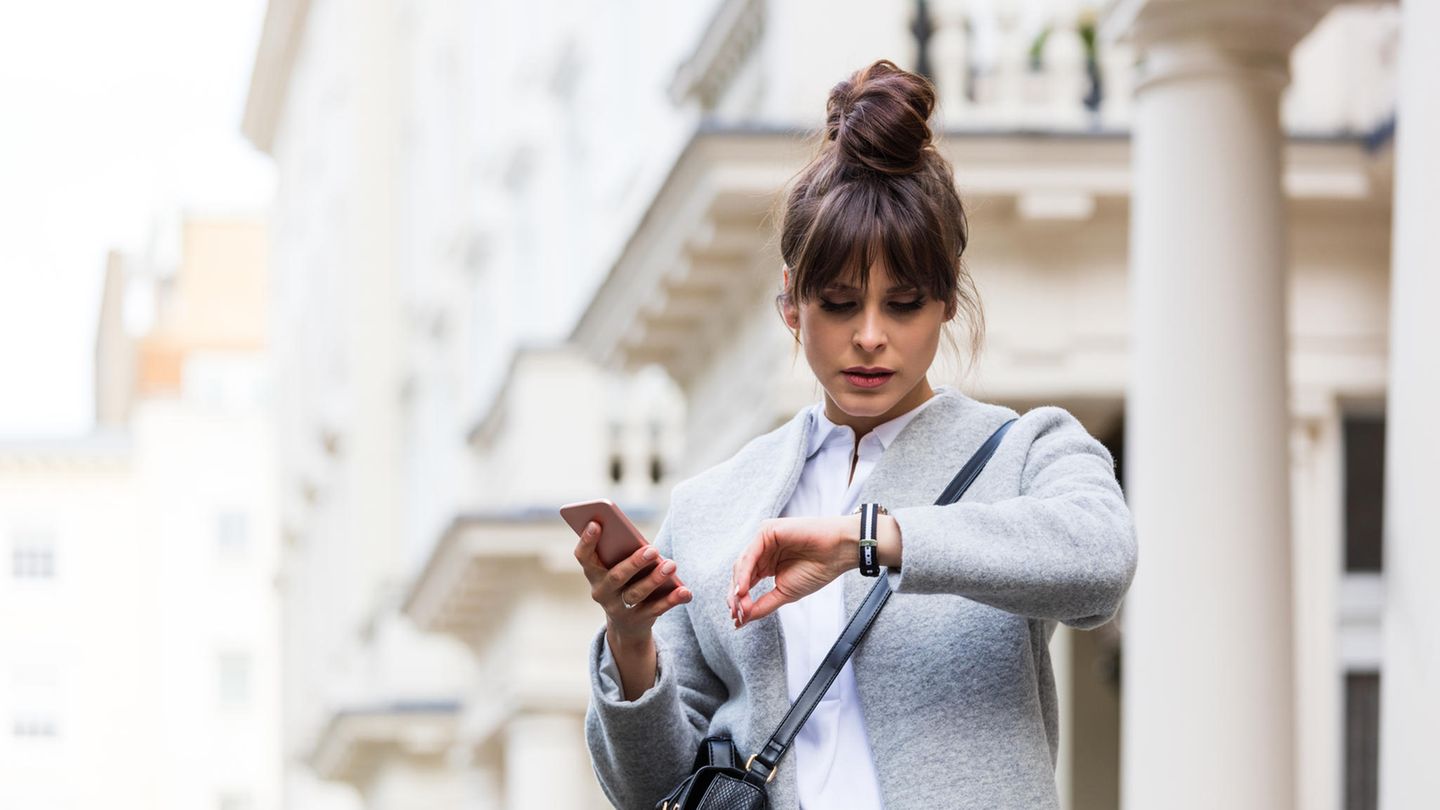 Freizeitstress: Frau hat ihr Handy in der Hand und schaut auf die Uhr Freizeitstress: Frau hat ihr Handy in der Hand und schaut auf die Uhr