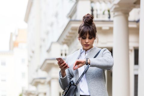 Freizeitstress: Frau hat ihr Handy in der Hand und schaut auf die Uhr