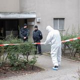 Polizisten stehen am Eingang eines Mehrfamilienhauses in Berlin, ein Polizist in Schutzanzug steht an einem Absperrband