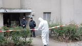 Polizisten stehen am Eingang eines Mehrfamilienhauses in Berlin, ein Polizist in Schutzanzug steht an einem Absperrband