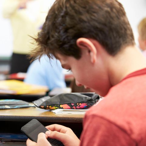 Handyverbot an Schulen  Handyverbot an Schulen: Junge schaut während des Unterrichts heimlich auf sein Handy