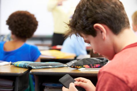Handyverbot an Schulen: Junge schaut während des Unterrichts heimlich auf sein Handy