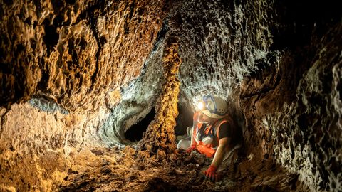 Ein Höhlenforscher mit leuchtender Lampe auf dem Helm kriecht durch einen Lava-Tunnelgang
